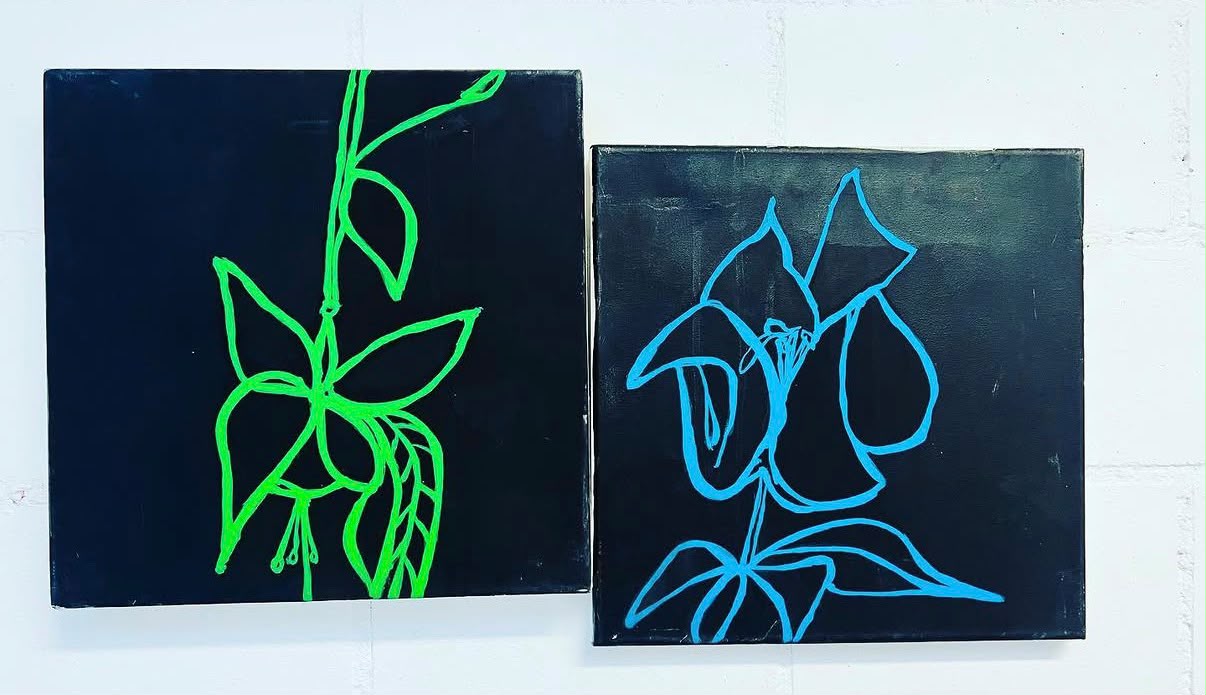 Zwei quadratische Leinwände auf weißer Backsteinwand – auf schwarzem Grund je eine Blüte als Linienzeichnung, links in Neongrün, rechts in Leuchtblau